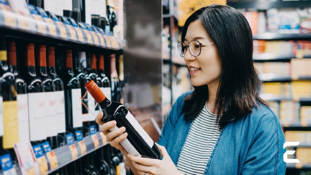 A woman examines a bottle of wine in a store.