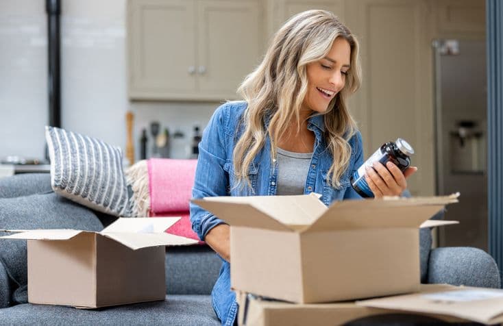 Smiling woman unboxing a package and holding up a dark bottle.